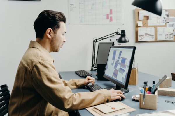 A product designer working at a modern office desk, focused on 3D designs on computer displays.